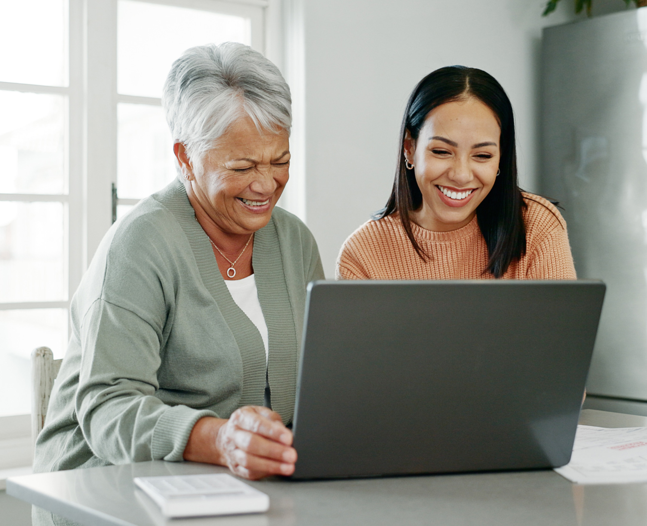 Young woman and older woman smiling while working together on a laptop.
